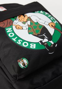 Black backpack featuring a Boston Celtics logo with a cartoon leprechaun in green and brown, accented by a small round logo on the side.