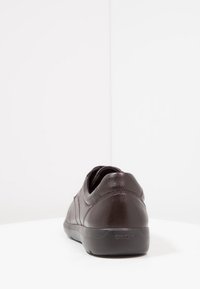 Donkerbruin leren casual schoen gezien vanuit de achterkant, met stiksels en merkzool zichtbaar op een witte ondergrond en achtergrond.