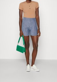 Maglietta aderente marrone chiaro e pantaloni corti in chambray blu. Borsa verde con un design strutturato, sneakers bianche. Linee semplici e pulite.