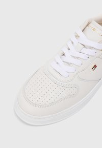 Basket en toile blanche de Tommy Hilfiger avec un bout perforé, des lacets blancs et un petit logo métallique sur le côté, vue de l'angle supérieur avant.