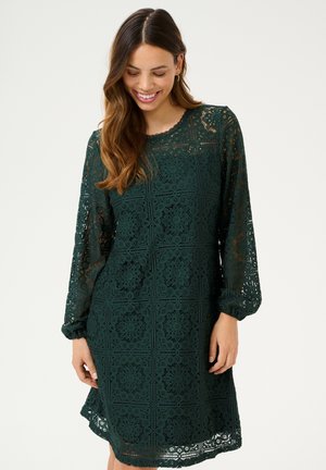 Green lace dress featuring a floral pattern, long sheer sleeves, and a scalloped neckline. The fabric has a delicate, textured appearance.
