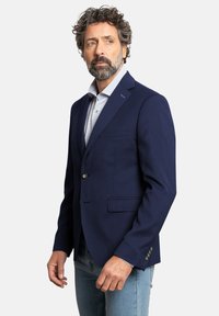 Blazer de color azul marino hecho de tela texturizada, con un solo botón, dos bolsillos frontales y solapa con muesca, combinado con una camisa de patrón claro.