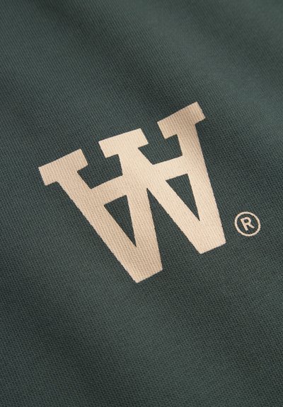Tissu vert arborant un grand logo "W" de couleur crème avec un symbole de marque déposée, surface texturée avec un motif subtil.