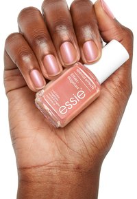 Bouteille de vernis à ongles Essie avec une forme carrée, en verre transparent, couleur rose pâle, bouchon blanc ; main affichant des ongles avec une finition rose clair scintillante.