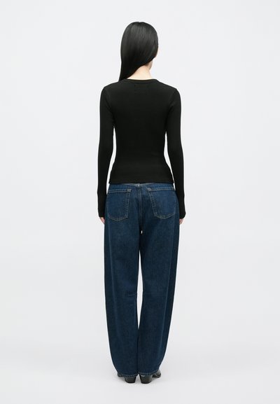 Μαύρο μακρυμάνικο τοπ με ραβδώσεις, συνδυασμένο με μπλε τζιν παντελόνια ψηλόμεσα, άνετης γραμμής. Η εμφάνιση απεικονίζεται από πίσω.