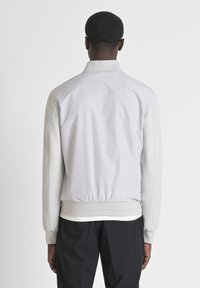 Lichtgrijze bomberjack met elastische manchetten en tailleband. Gladde stof met een semi-matte afwerking en contrasterende lichtbeige mouwen.