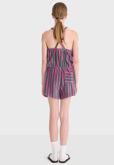 Enfant vu de dos portant une combinaison sans manches rayée rose et verte avec une poche arrière, des chaussettes blanches et des sandales noires.