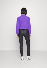 Topa larga de manga con textura en color púrpura y hombros fruncidos, combinada con pantalones negros ajustados y botines de tacón blanco.