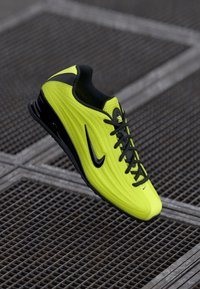 Neoonkollane ja must sportlik king, mille paelad rippuvad metallvõrgust põranda kohal.