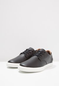 Black leather shoes with a smooth finish, featuring a white rubber sole and black laces, designed with minimal stitching details and a rounded toe.