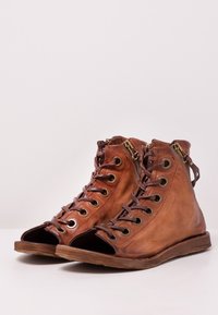 Hnědé kožené kotníkové boty s otevřenou špičkou, kovovými očky, hnědými tkaničkami a bočním zipem. Mají plochou dřevěnou podrážku a texturovaný povrch.
