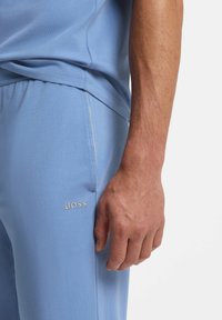 Haut et pantalon décontractés bleu clair en tissu doux. Présente un logo "BOSS" brodé en blanc sur la jambe du pantalon. Détails de couture subtils visibles.