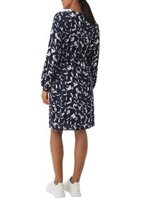 Robe marine avec un motif abstrait blanc, manches longues et taille cintrée. Associée à des baskets blanches, elle a une coupe mi-genoux.