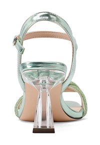 Sandalo con tacco alto metallizzato verde menta, dotato di tacco geometrico trasparente e dettagli in perline sui lati. Schiena aperta con cinturino alla caviglia regolabile.