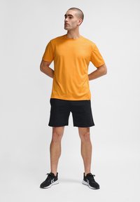 Kortärmad, orange sportt-skjorta i fukttransporterande tyg, tillsammans med svarta sportshorts. Har en diskret logotyp på bröstet.
