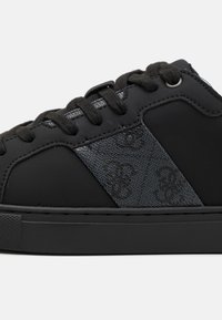 Černé tenisky s texturovanou černou částí s jemným vzorem, zaoblenou špičkou a černými tkaničkami. Gumová podrážka s plochým designem.