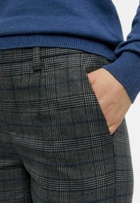 Gray plaid trousers with a textured fabric, featuring blue and black check patterns; pocket detail visible, worn with a blue sweater.