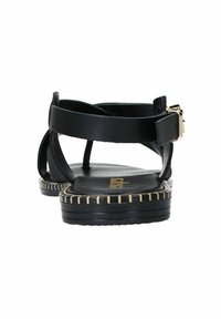 Sandales en cuir noir avec une semelle plate, dotées de brides entrecroisées et d'une boucle dorée. La semelle présente un motif de surpiqûre.