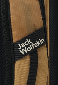 Jack Wolfskin Rucksack aus strukturiertem, braunem Stoff, mit schwarzen Netz-Akzenten und einem weißen Logoetikett, das an die Seite genäht ist.