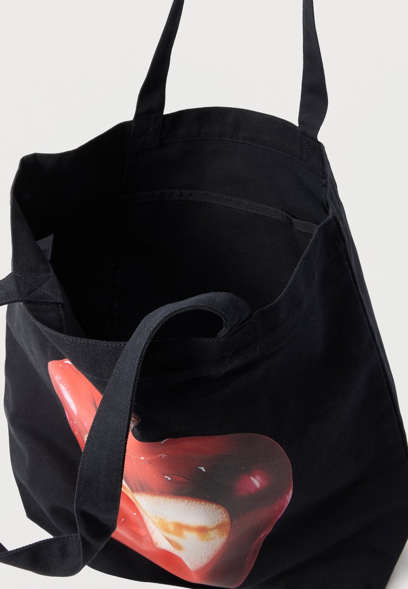 Schwarze Segeltuchtasche mit langen Griffen und einem grafischen Aufdruck einer roten und weißen abstrakten Form auf der Vorderseite.