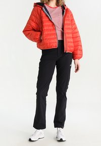 Red puffer jacket with a hood, featuring a zip closure and ribbed cuffs, worn over a striped shirt and black pants, with white athletic shoes.