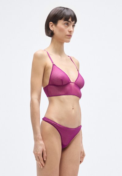 Magenta fehérnemű szett, mely egy hálós bralette-et tartalmaz állítható pántokkal és hozzáillő alsót, mindkettő texturált mintázattal és hullámos szegéllyel.