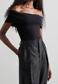 Top nero aderente off-the-shoulder con texture a righe. Abbinato a pantaloni grigi a vita alta con pieghe e tasche laterali.