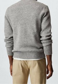 Suéter gris con relieve, mangas largas, cuello redondo y acabado texturizado, combinado con pantalones beige. El suéter tiene un ajuste ceñido al cuerpo.