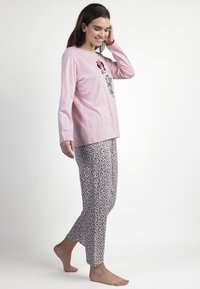Top de manga larga rosa con un diseño gráfico, combinado con pantalones de pijama con estampado de leopardo en blanco y marrón. La modelo está descalza y de pie, mirando hacia la izquierda.