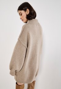 Beige Übergröße Pullover mit hohem Rippkragen, überschnittenen Schultern und gerippten Bündchen. Weicher Stoff und lockere Passform. Keine auffälligen Muster oder Akzente.