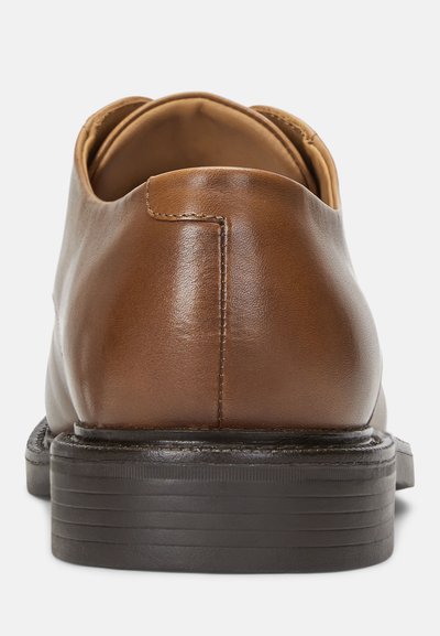Brune lærdress sko med en glat finish, afrundet bag, og en flad sort gummisål med lineære mønstre.