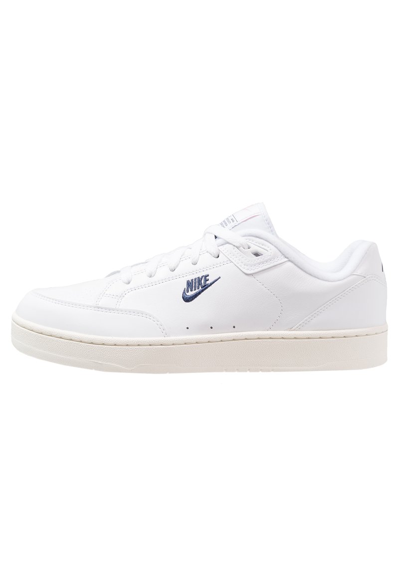 Baskets en cuir blanc avec une texture lisse, dotées d'un logo Nike bleu, de lacets plats et d'une semelle en caoutchouc beige. Design minimaliste.