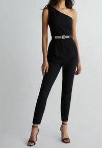 Mono negro sin mangas con un corpiño ajustado, piernas ajustadas y un cinturón adornado con rhinestones. Presenta una textura suave y líneas limpias.