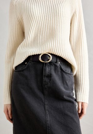 Cream ribbed sweater tucked into a black denim skirt, featuring a gold circular buckle belt. The texture is soft and casual.