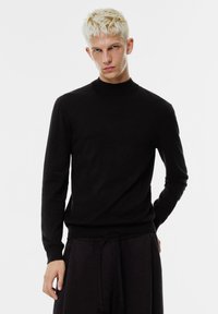 Svart polotröja i mjukt tyg med långa ärmar och en figurnära silhuett, kombinerad med mörka byxor för en monokrom look.