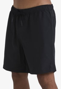 Shorts de bain noirs avec une taille élastique et un cordon de serrage, dotés d'une poche latérale et d'une petite étiquette de logo sur l'ourlet. Texture lisse.
