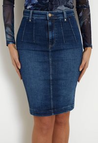 Jeans-Bleistiftrock in dunkler Waschung mit vorderen Falten, einem Reißverschluss und dezenten Stickdetails. Geschmeidige Textur und taillierte Passform.