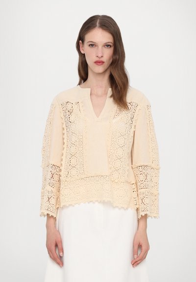Beige bluse med indviklet blonderdetalje, V-hals og løse, lange ærmer med strukturerede mønstre og bølgede kanter.
