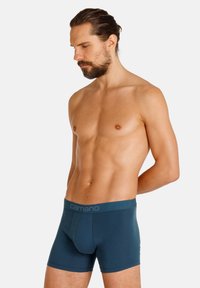 Boxershorts in donkerteal stof met een getailleerd ontwerp. Voorzien van een zachte elastische tailleband met het label "camano." Gladde textuur, lengte tot halverwege de dijen.