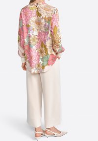 Blusa floral abotonada en rosa y crema, con grandes flores, mangas largas y tejido ligero; combinada con pantalones de pierna ancha en crema.