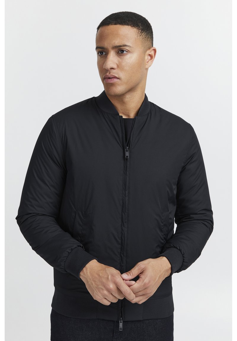 Giacca bomber nera realizzata in materiale liscio e imbottito con zip frontale, polsini e orlo a costine; presenta tasche laterali e un colletto rotondo.