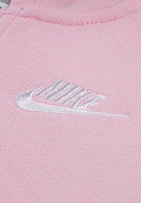 Υλικό ροζ φούτερ με λεία υφή και λευκό κεντητό λογότυπο της Nike. Το σχέδιο περιλαμβάνει διακριτικές λεπτομέρειες ραφής.