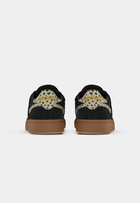 Čierne semišové tenisky s leopardím vzorom na päte a gumovou podrážkou. Zadná časť obsahuje zlaté branding "Reebok" a športové dizajnové akcenty.