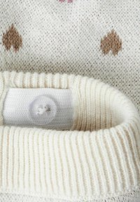 Détail d'un pull en tricot couleur crème avec un col côtelé, un tissu texturé et de petits motifs en cœur marron et rose. Bouton clair visible.
