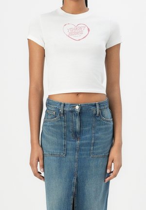 Camiseta corta blanca con un logotipo de corazón "TOMMY JEANS" en color rosa. Combinada con una falda de mezclilla azul de talle alto con una abertura frontal.