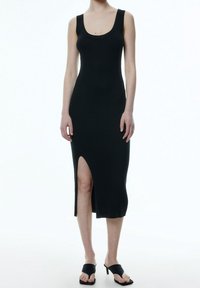 Svart randig midiklänning med rundad halsringning och sidoklyfta; åtsittande form som framhäver texturen. Buren med svarta slidesandaler.