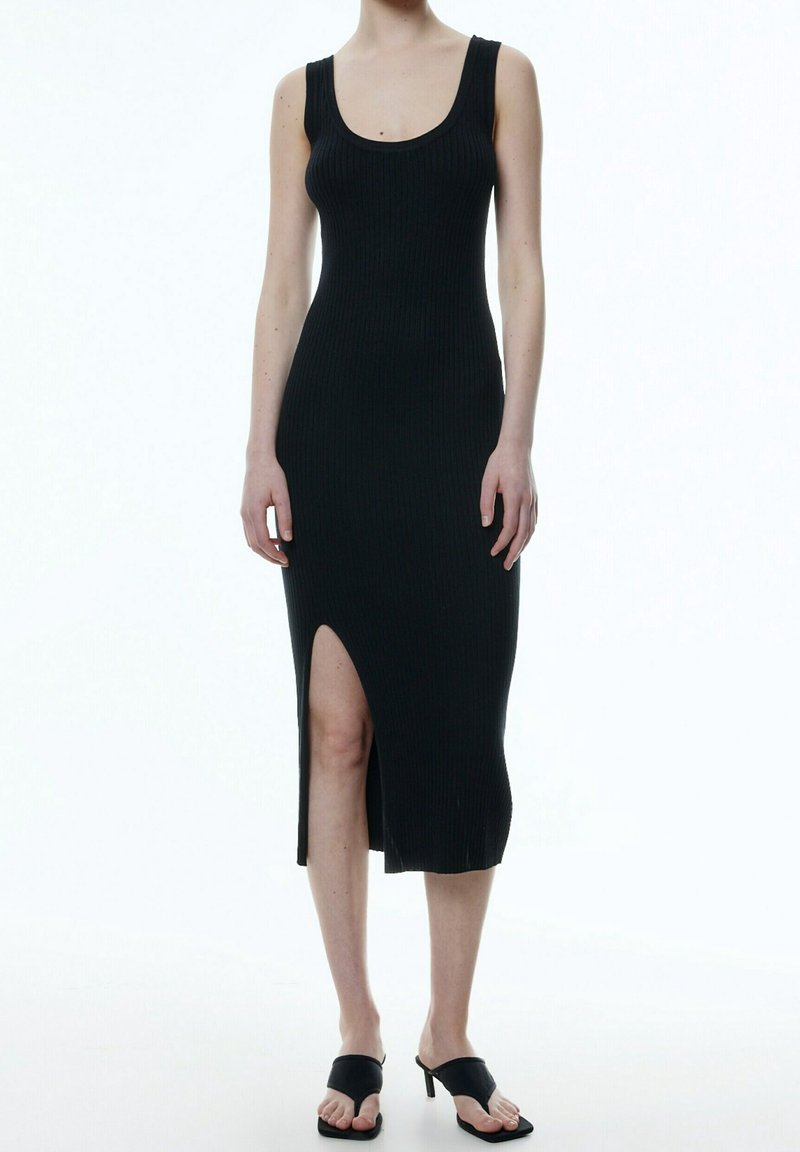 Svart randig midiklänning med rundad halsringning och sidoklyfta; åtsittande form som framhäver texturen. Buren med svarta slidesandaler.