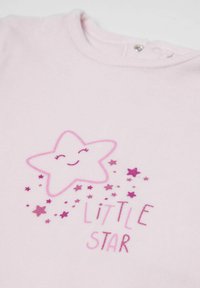 Jasnoróżowa bawełniana koszula z grafiką uśmiechniętej gwiazdy i napisem "MAŁA GWIAZDA" w różnych odcieniach różu.