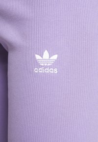 Lavendelfärgade ribbade leggings med en vit broderad Adidas-logotyp nära övre vänstra delen. Mjuk textur och åtsittande design.