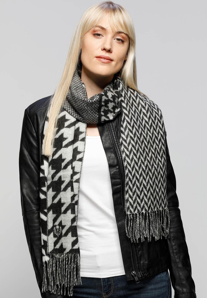 Sort-hvid mønstret tørklæde med et houndstooth-design på den ene side og et zigzag-mønster på den anden; afsluttet med frynser.